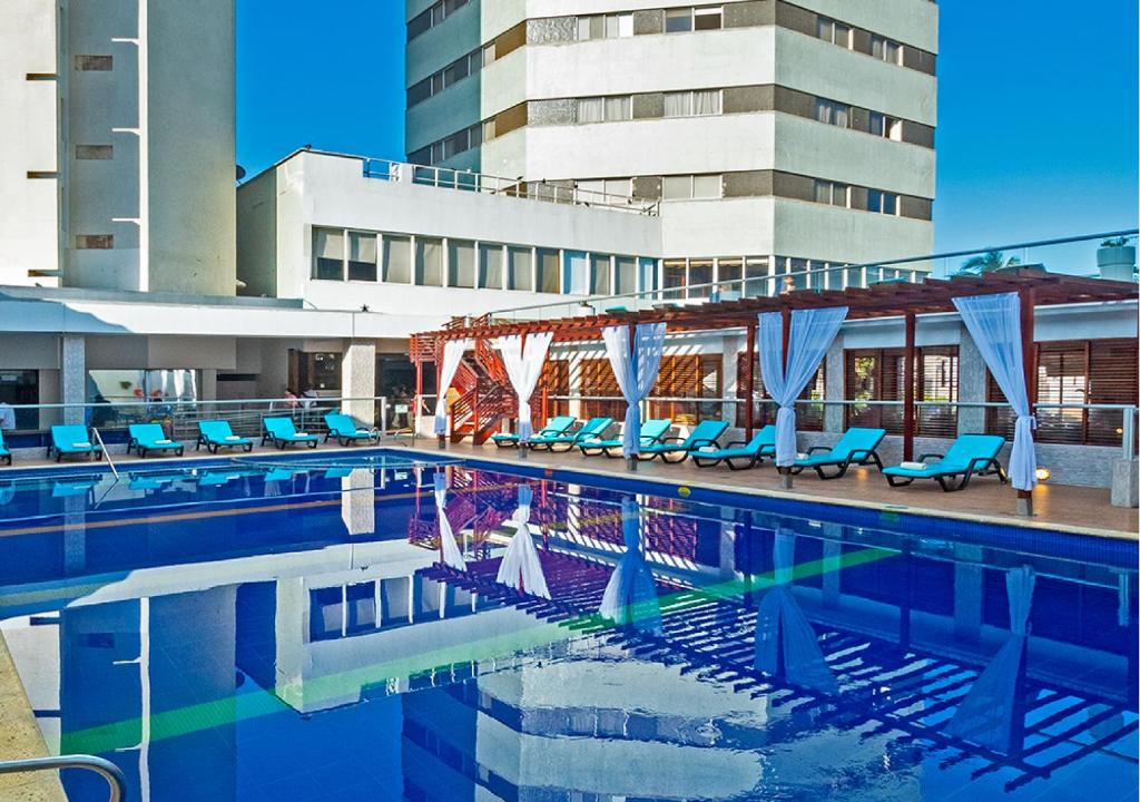 uma piscina com cadeiras azuis e um edifício em Hotel Dorado Plaza Bocagrande em Cartagena das Índias