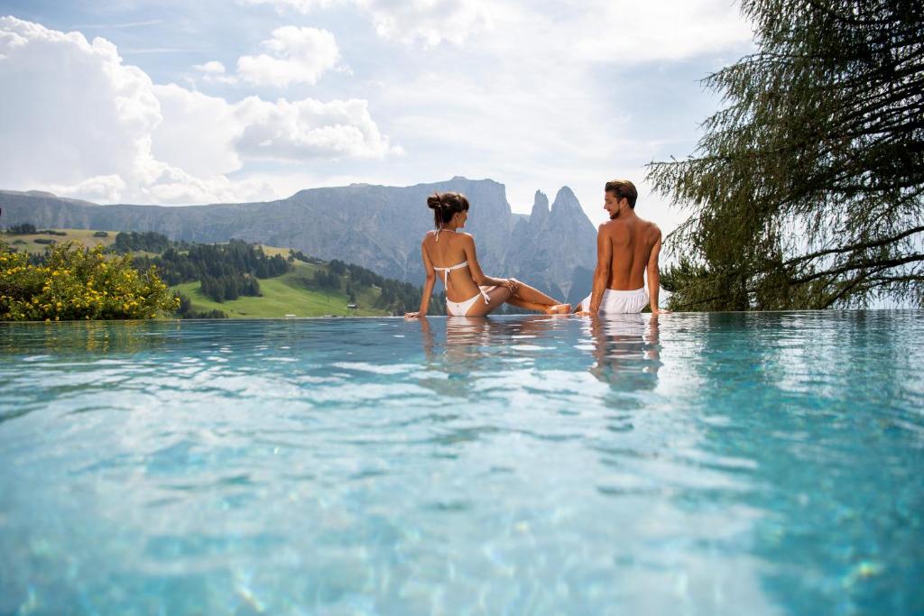 un hombre y una mujer sentados en el agua en una piscina infinita en Hotel Rosa Eco Alpine Spa Resort, en Alpe di Siusi