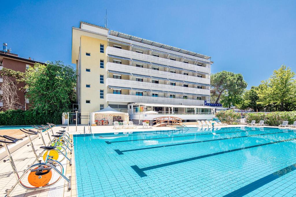 una piscina con sedie e un grande edificio di Aparthotel Albatros a Lignano Sabbiadoro