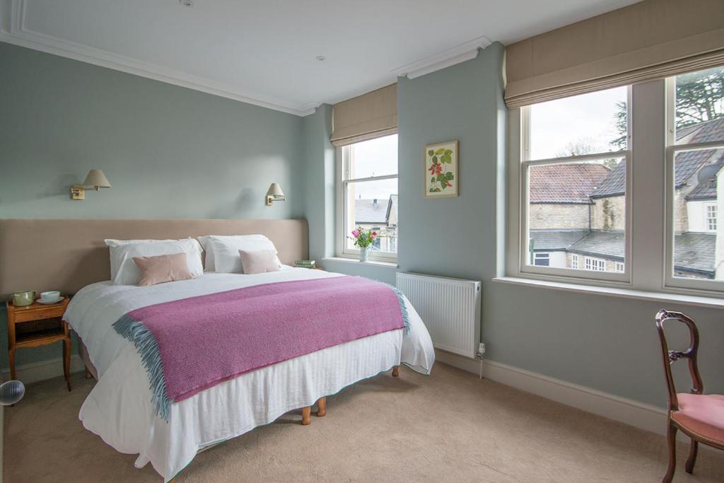 een slaapkamer met een bed met een paarse deken en 2 ramen bij Bistro Lotte in Frome