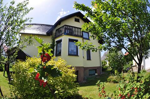 a yellow house with a balcony on top of a yard at Ferienwohnung Glasperlenfloh in Ilmenau