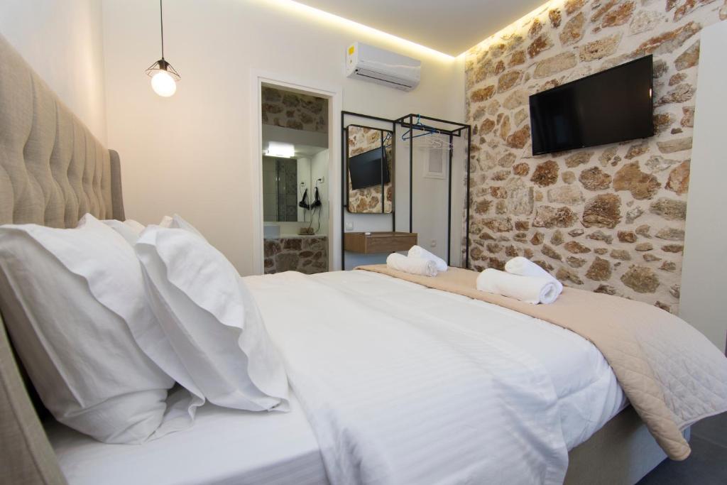 a bedroom with a white bed with a tv on a stone wall at Acrothea Perdika in Perdika