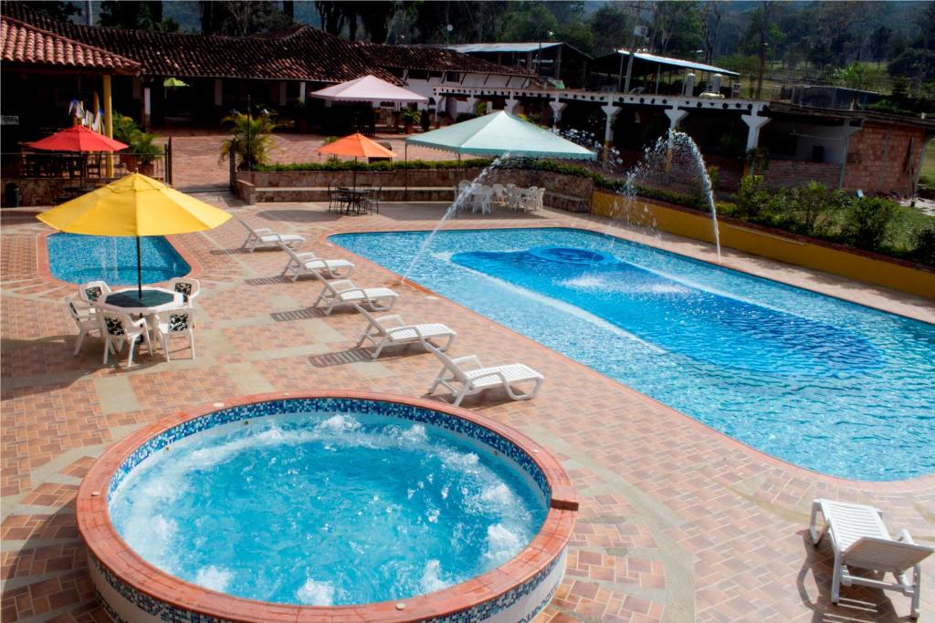 a swimming pool with chairs and umbrellas and a pool at Hotel Hacienda Santa Barbara in San Gil