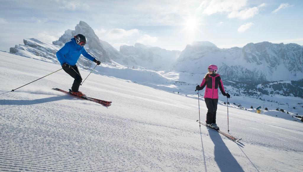two people are skiing down a snow covered slope at Adler Spa Resort Dolomiti in Ortisei