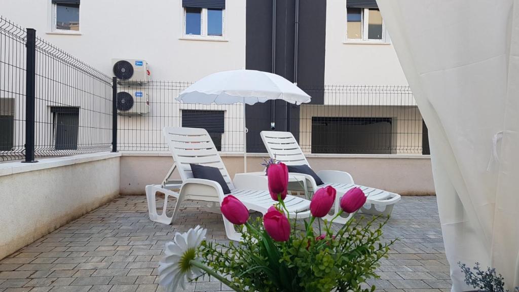 3 Stühle und ein Regenschirm auf einem Balkon mit Blumen in der Unterkunft Apartments BRIST HILLS in Pula
