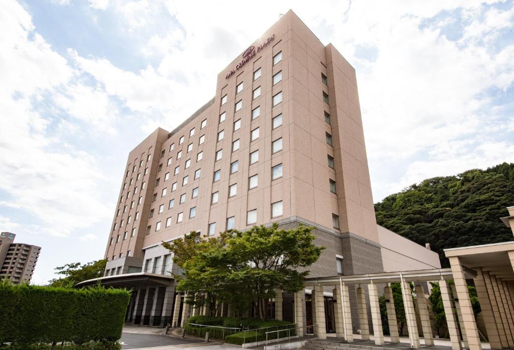 ANA Crowne Plaza Yonago, an IHG Hotel في يوناغو: مبنى ابيض طويل وامامه شجرة