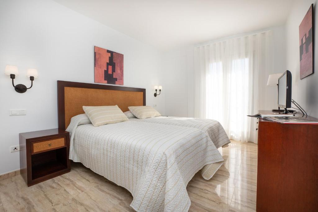 a white bedroom with a bed and a television at Apartamentos Jimmy in Nerja