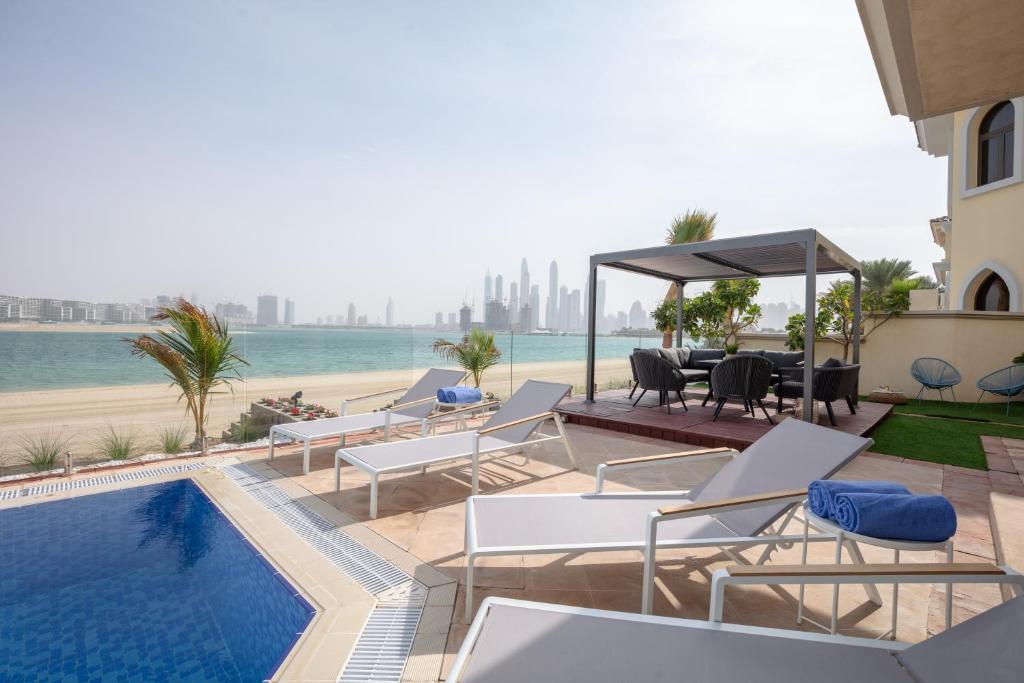 een patio met een zwembad en stoelen en een tafel bij Stella Stays Gorgeous 5 BDR Palm Villa Beach Private Pool in Dubai
