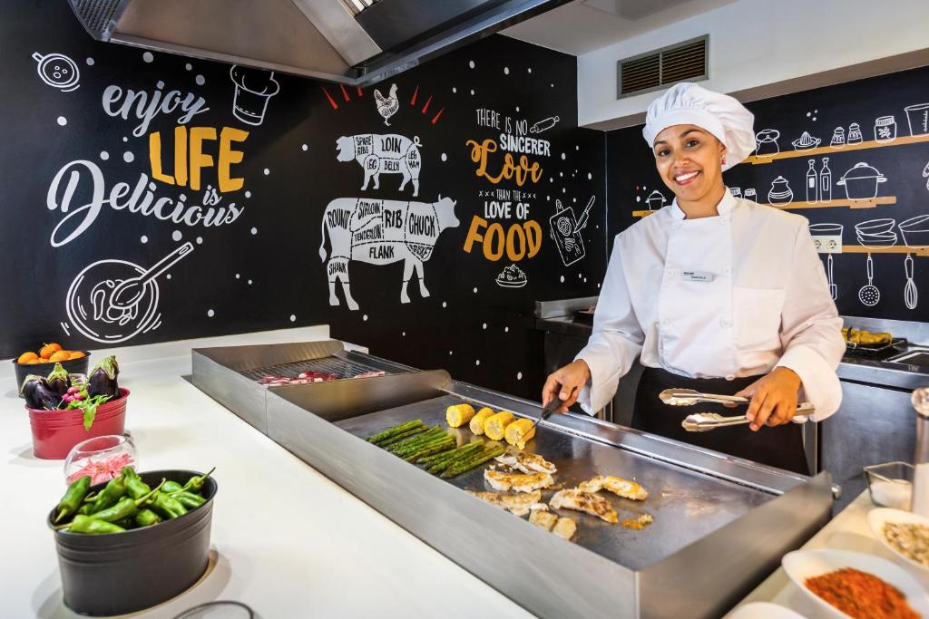 a woman in a kitchen preparing food on a grill at Barceló Corralejo Sands in Corralejo