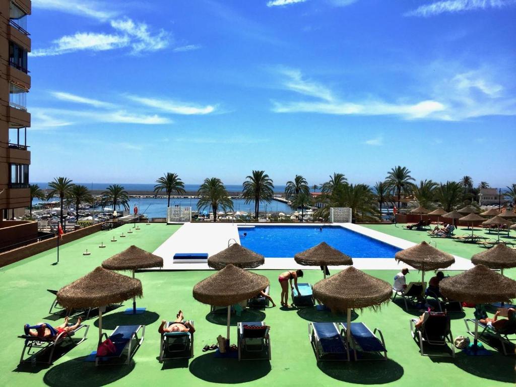 a pool with chairs and umbrellas and the ocean at Las Palmeras, 893 in Fuengirola