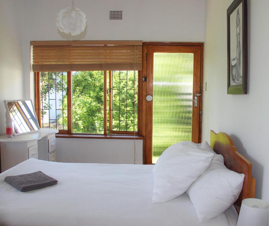 a bedroom with a bed with white sheets and a window at Norfolkden Beachhouse in Hermanus
