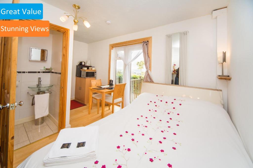 Un dormitorio con una cama blanca con flores rojas. en Cosy Snug with shower ensuite - It has beautiful countryside views - Only 3 miles from Lyme Regis, Charmouth and River Cottage - It has a private balcony and a real open fireplace - Comes with free private parking, en Axminster