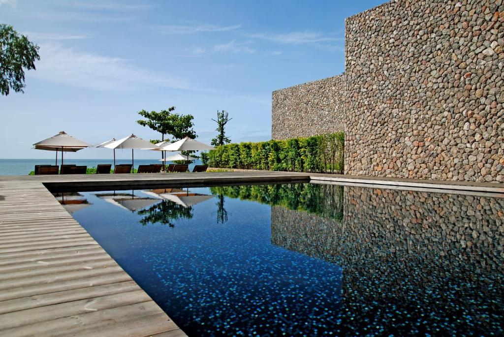 a swimming pool in front of a building with a stone wall at Tolani Resort Kui Buri in Kui Buri