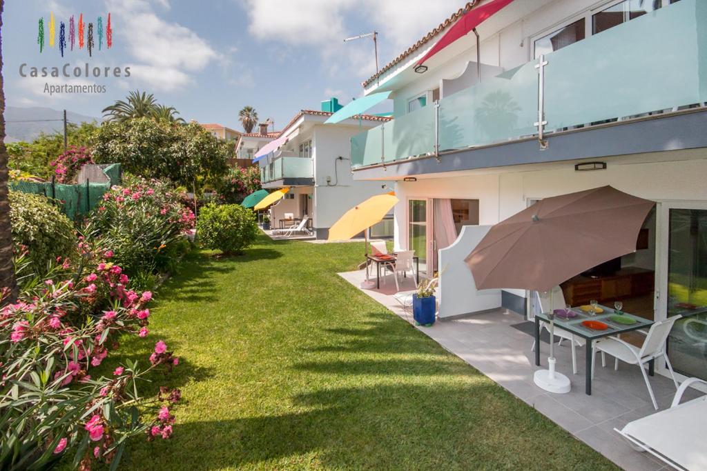 a garden with a table and an umbrella next to a building at CasaColores Apartamentos in Puerto de la Cruz