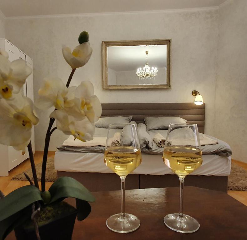 two glasses of wine on a table in front of a bed at Corte Apartman in Pápa
