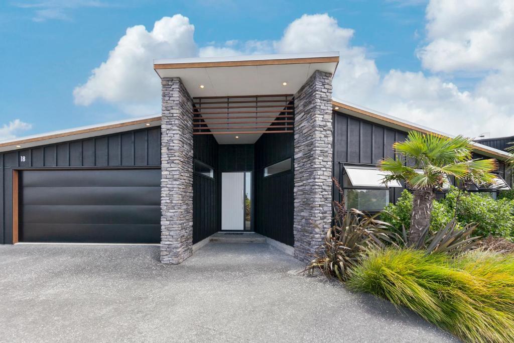 een huis met een zwarte garage en een palmboom bij Stylish Villa Escape - Matakana Holiday Home in Matakana