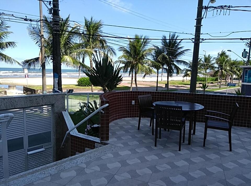 eine Terrasse mit Tisch und Stühlen sowie Strand in der Unterkunft Apto. De frente pro Mar in Praia Grande