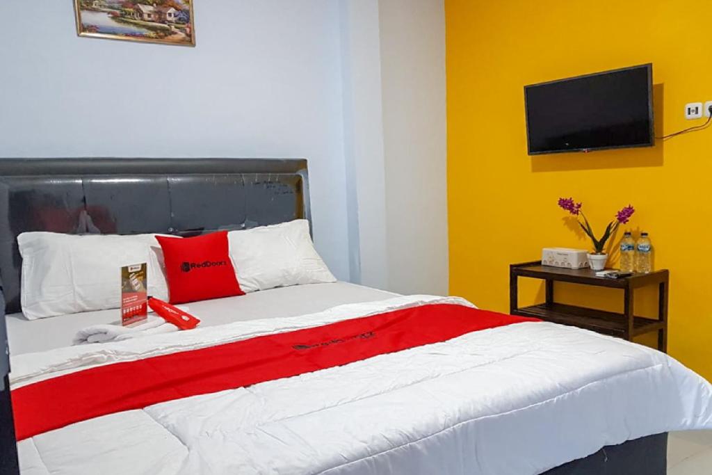 a bedroom with a red and white bed with a television at RedDoorz near RSUD Kota Luwuk in Luwuk