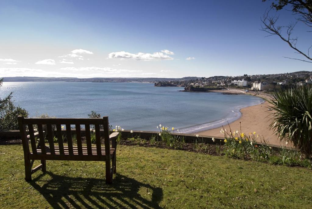 una panchina seduta sull'erba vicino a una spiaggia di Astor House a Torquay