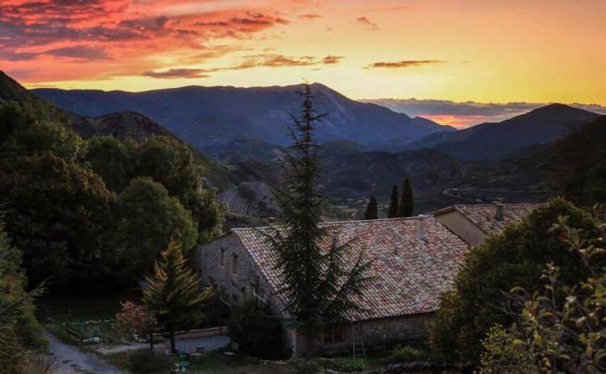 um pôr-do-sol sobre uma aldeia com montanhas ao fundo em Malia - Chambres d'hôtes & Gîte em Barret-de-Lioure