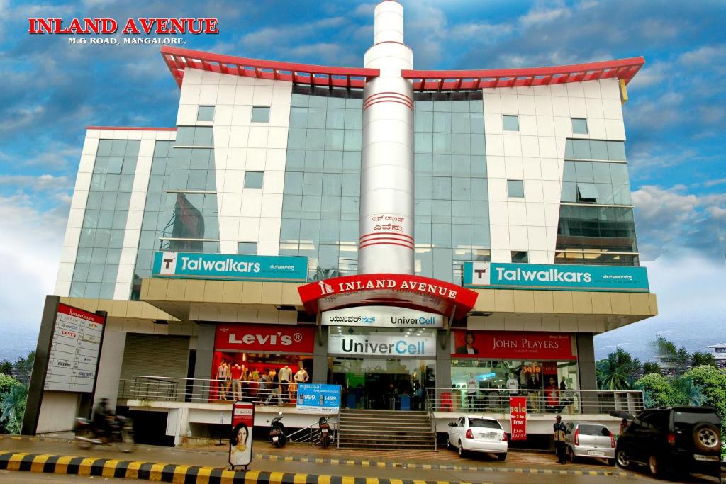un gran edificio con coches estacionados frente a él en Hotel Inland Avenue, en Mangalore