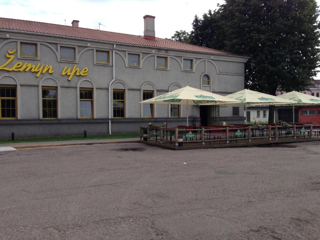 a building with tables and umbrellas in front of it at Žemyn upe in Kaunas