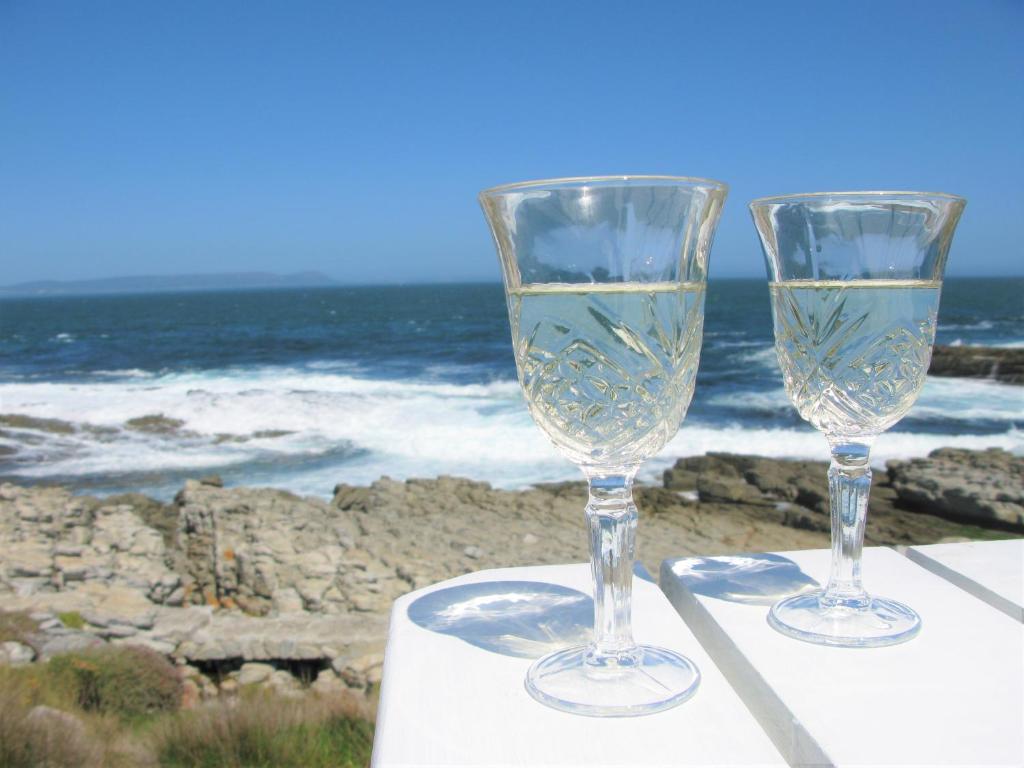 two wine glasses sitting on a table near the ocean at Beachfront Cottage - Hermanus Whale View in Hermanus