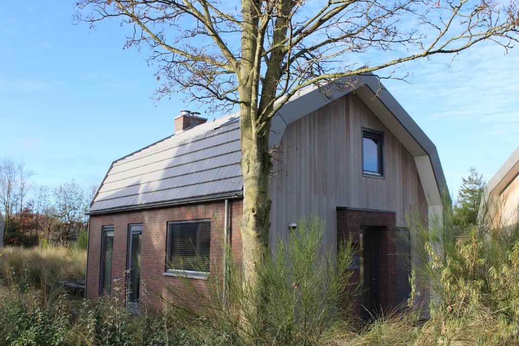 Une ancienne grange avec un arbre devant elle dans l'établissement Duinroos Egmond, à Egmond aan den Hoef