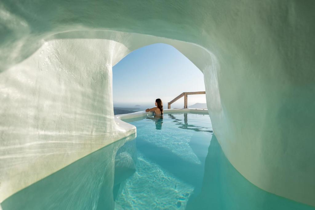 a woman is sitting in a swimming pool in an ice cave at Cocoon Suites in Imerovigli