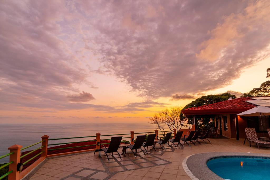 eine Terrasse mit Stühlen, einem Pool und dem Meer in der Unterkunft Villas Alturas in Dominical