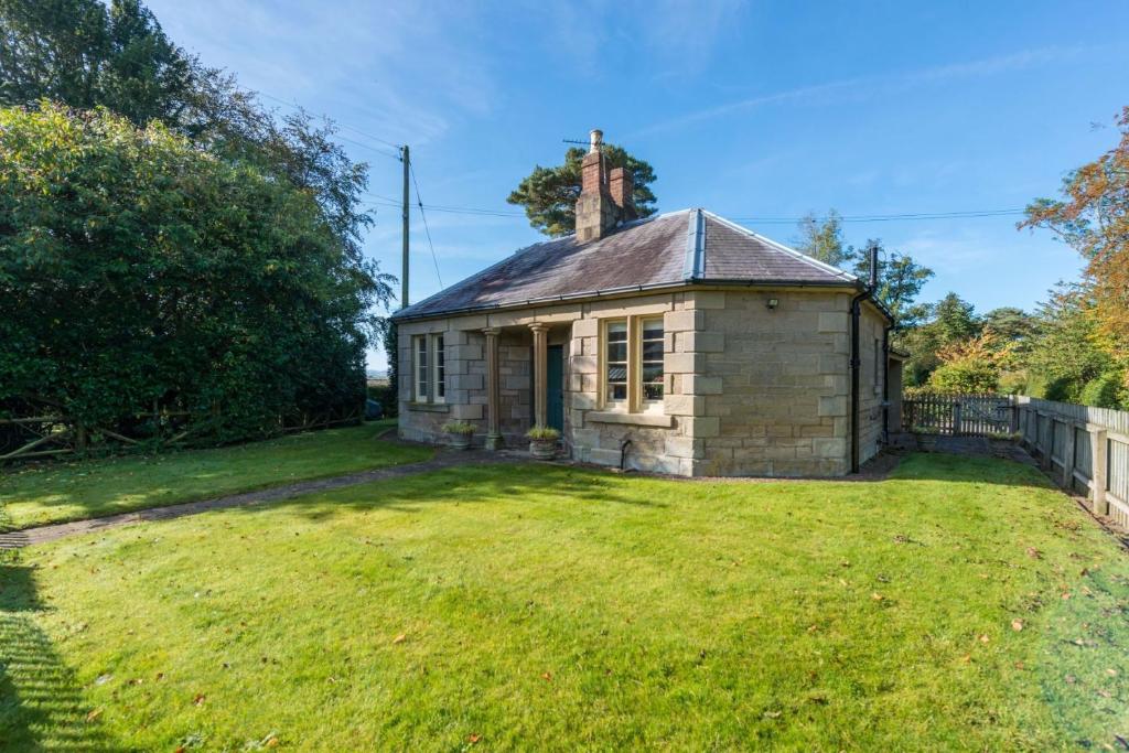 a small stone building in a yard with a grass field at Melkington Lodge in Cornhill-on-tweed