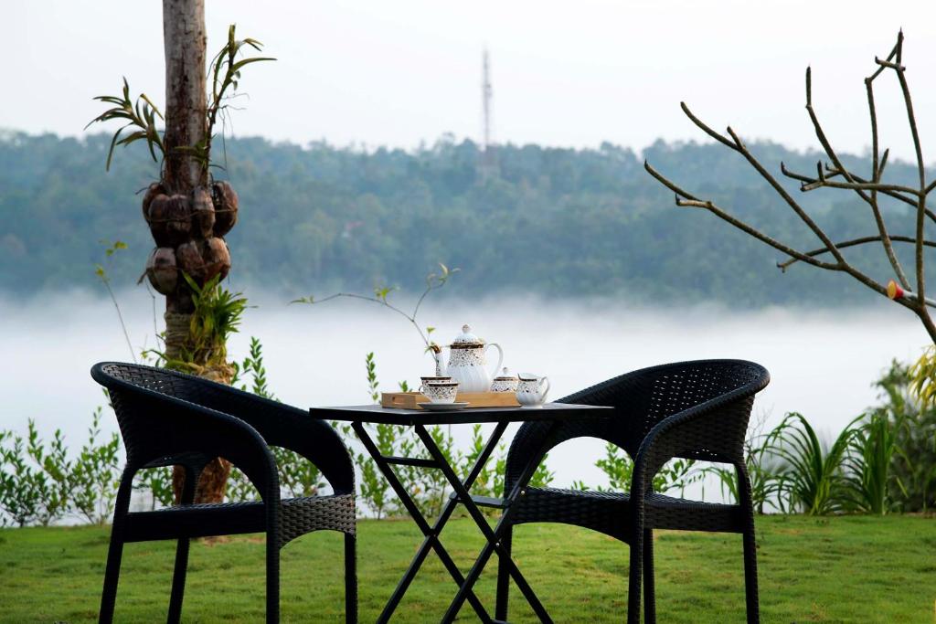 a table with two chairs next to a lake at StayVista at Novera The Lake Villa in Tariyod