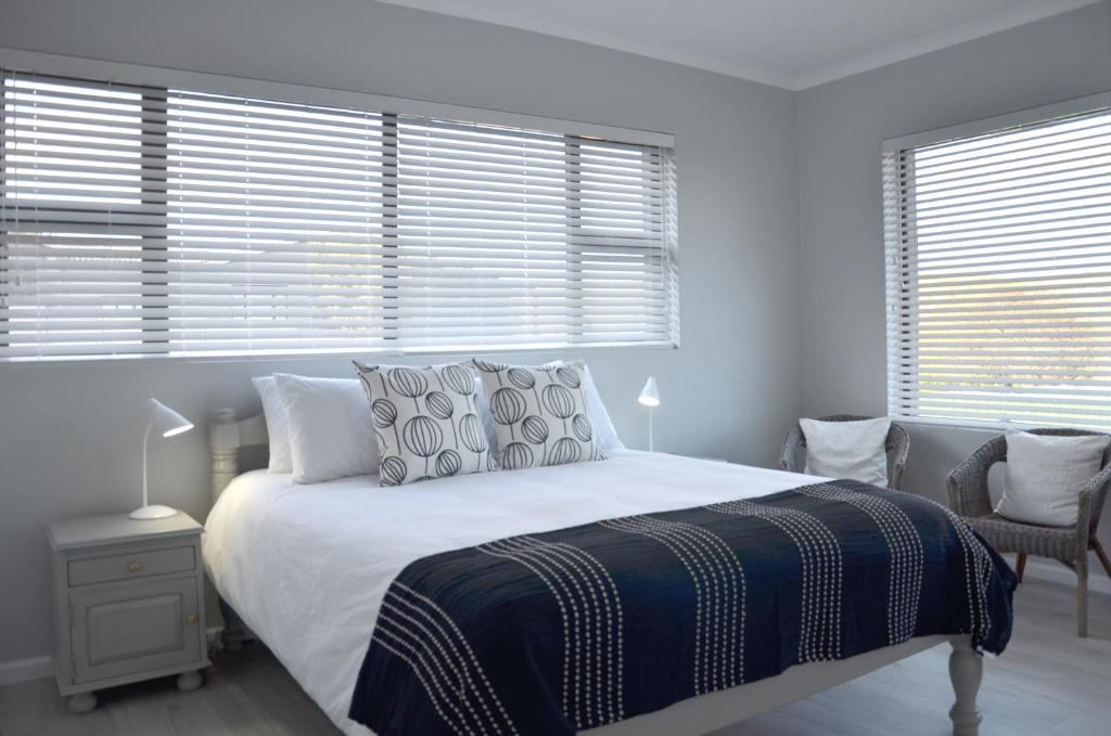 a bedroom with a white bed with a blue blanket and windows at Beach Blessings, Fun in the sun in Stilbaai