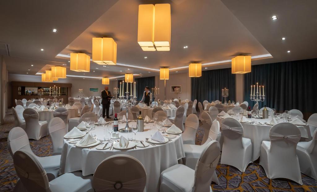 a banquet hall with white tables and white chairs at Maldron Hotel Belfast International Airport in Aldergrove