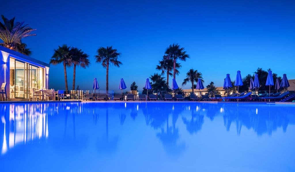 una piscina notturna con palme e un edificio di Solimar Aquamarine Resort a Gerani Chanion