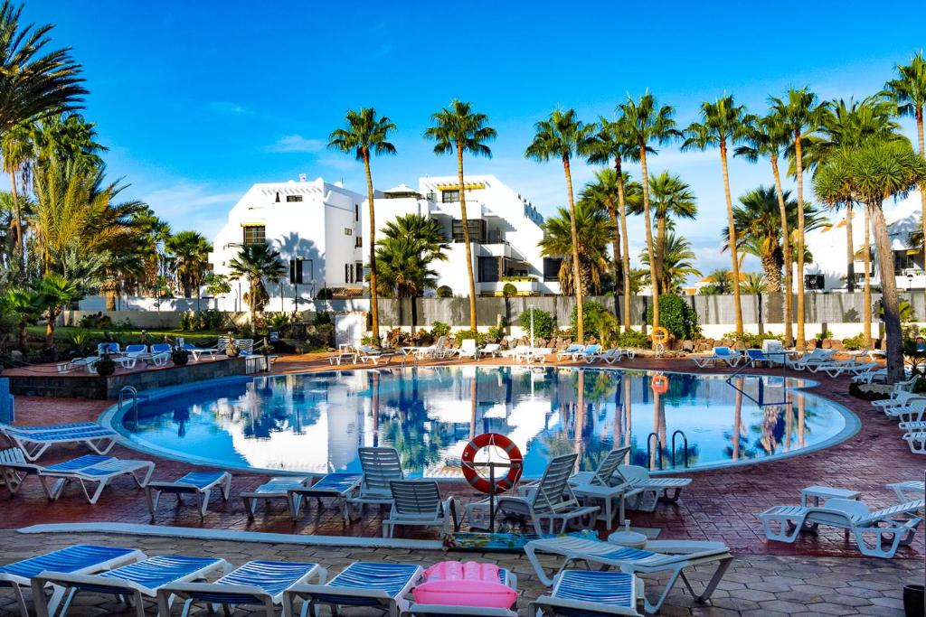 a pool at a resort with chairs and palm trees at Apartment El Dorado, Las Americas in Arona