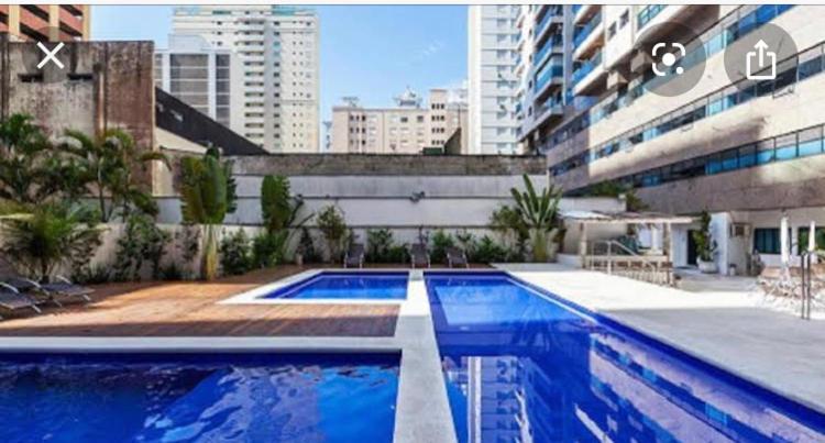 einem großen blauen Pool vor einem Gebäude in der Unterkunft APTO CHURRASQUEIRA, Capitania Varam, Pitangueiras, piscina, 100 m da praia, 2 dormitórios, 2 vagas de garagem in Guarujá