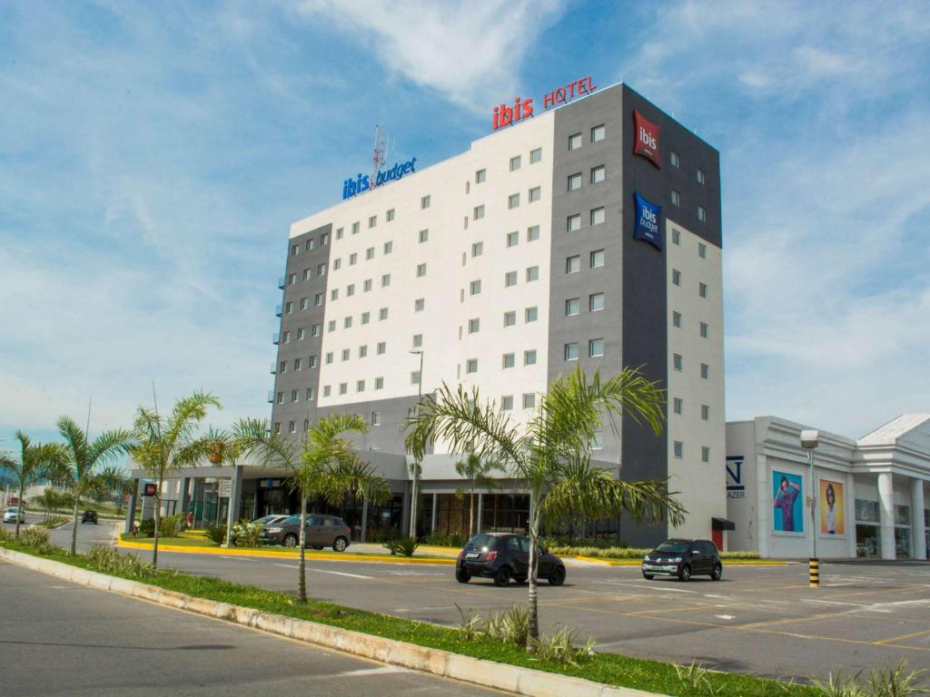 a large white building with cars parked in a parking lot at Ibis Budget Lorena - Circuito da Fé in Lorena