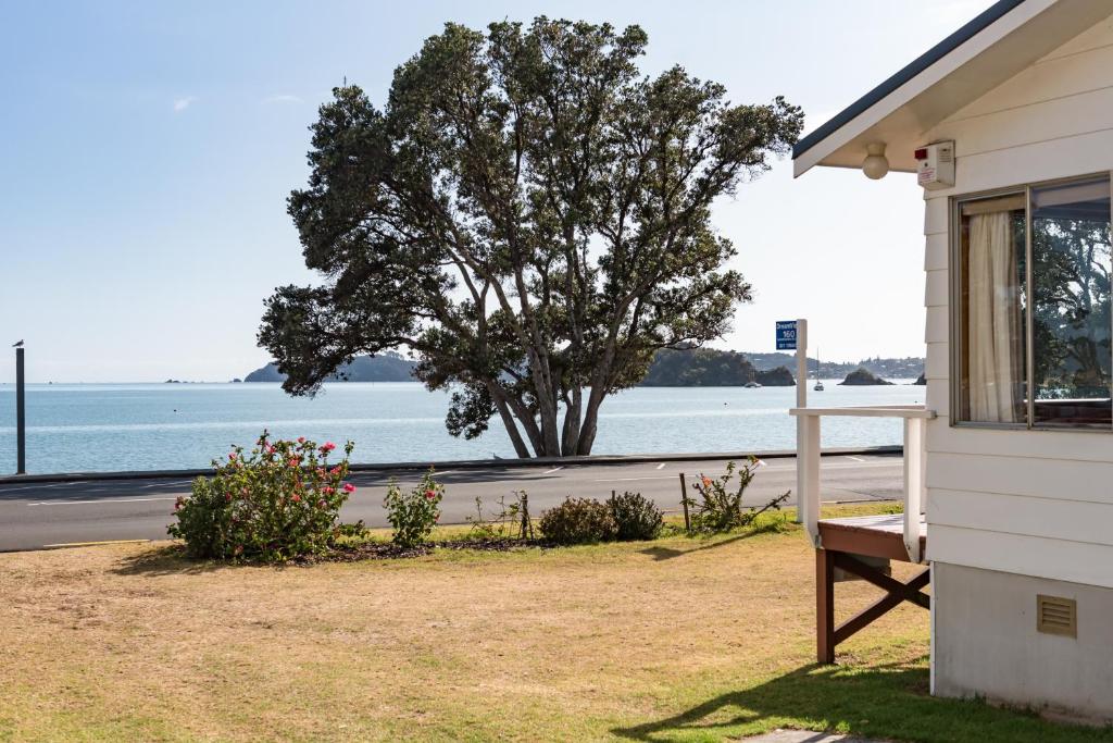 a house with a window and a tree next to the ocean at Dream View Waterfront Paihia in Paihia