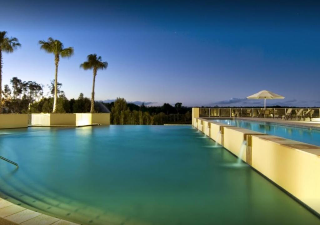 a swimming pool with blue water and palm trees at Pelican Waters Resort in Caloundra