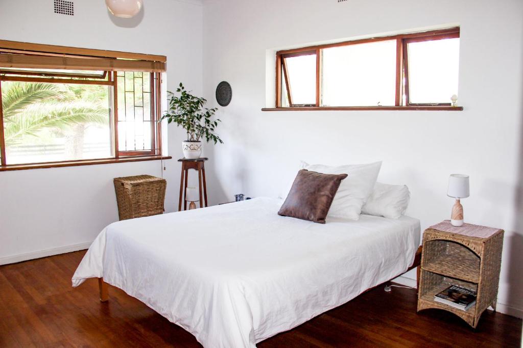 a bedroom with a white bed and two windows at Norfolkden Beachhouse in Hermanus
