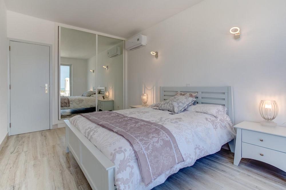 a white bedroom with a large bed and a mirror at Vila Gaivota 3G in Ferragudo