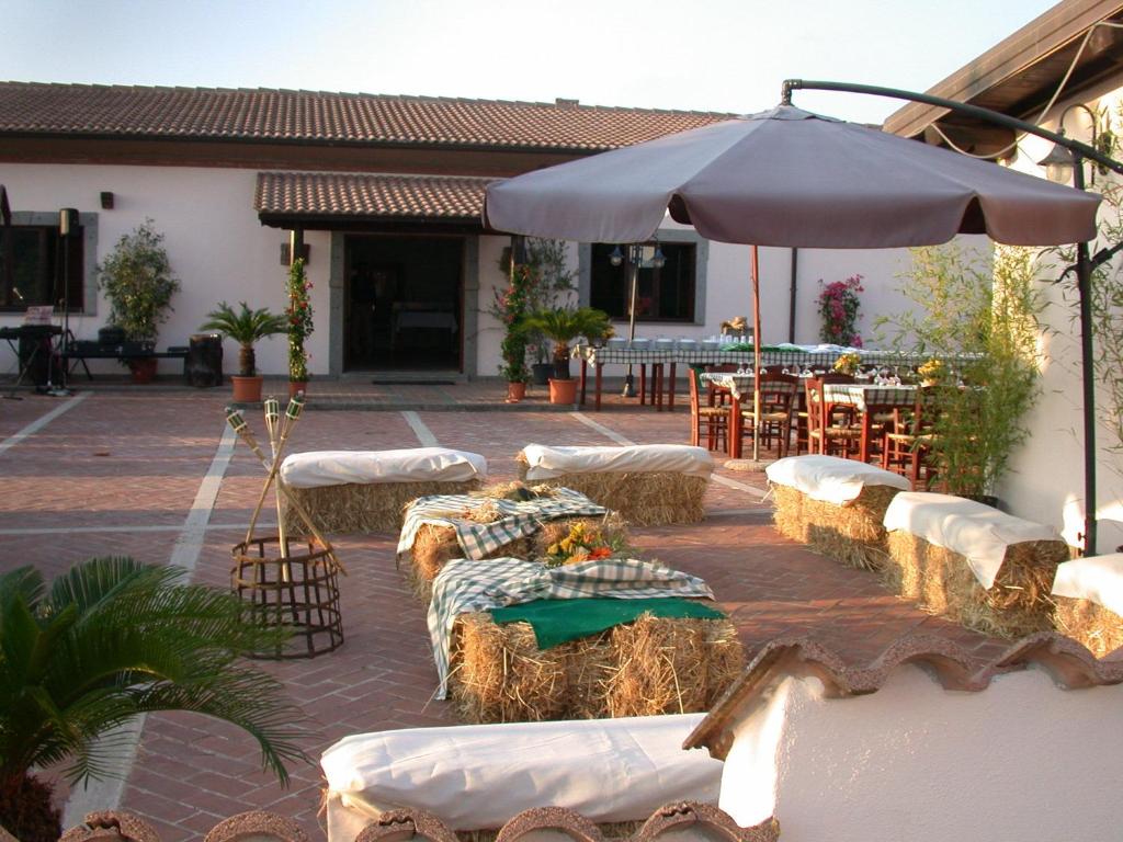 une terrasse avec des tables recouvertes de foin et un parasol dans l'établissement Agriturismo Torre Cristina, à Aprilia