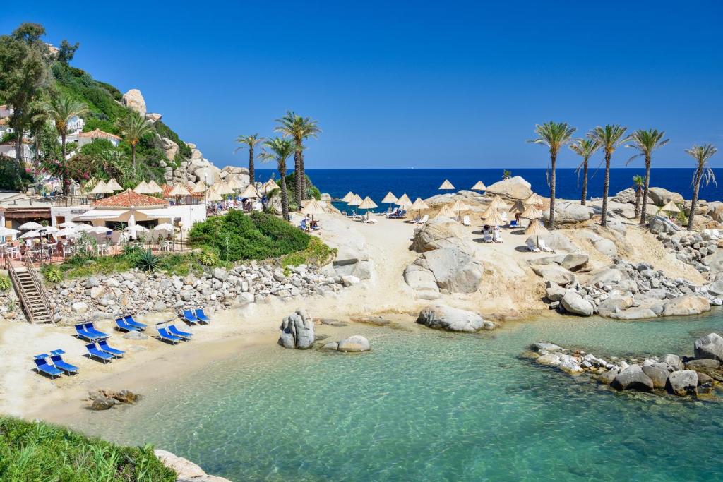 una spiaggia con sedie, palme e l'oceano di Arbatax Park Resort - Telis a Àrbatax