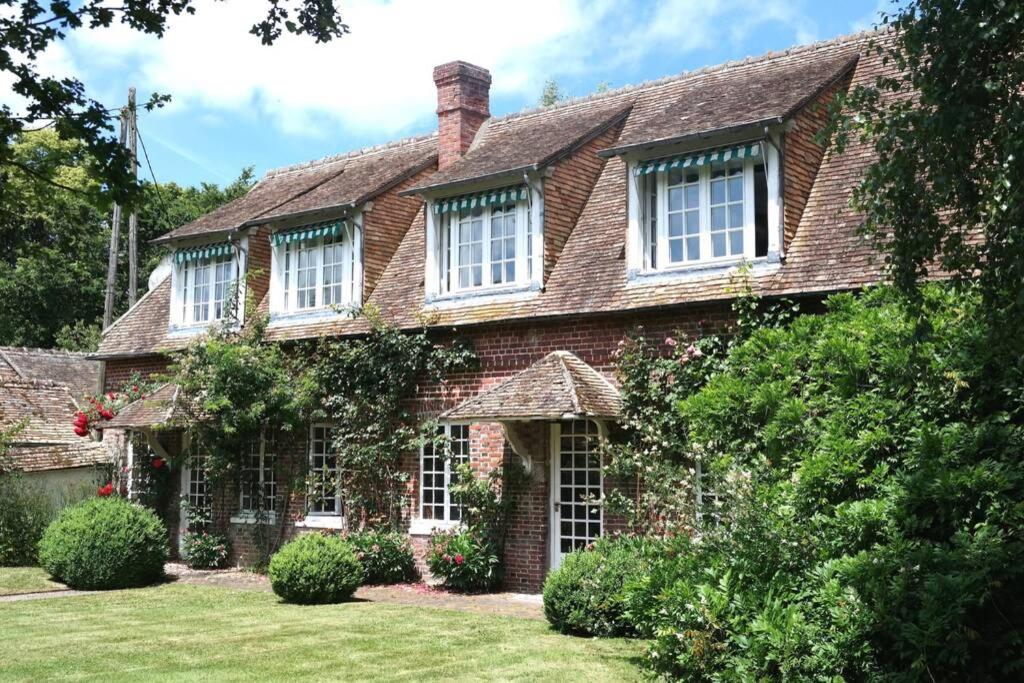 una antigua casa de ladrillo con ventanas blancas y arbustos en Cottage Normand en Montaure