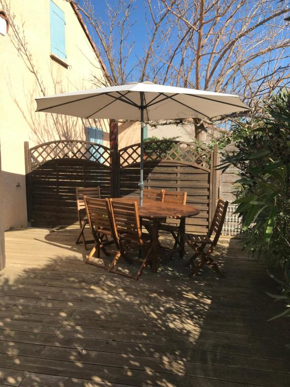 une table et des chaises en bois sous un parasol dans l'établissement Saint-Pierre-la-Mer - Narbonne Plage Location T3 Climatisée, à Saint Pierre La Mer