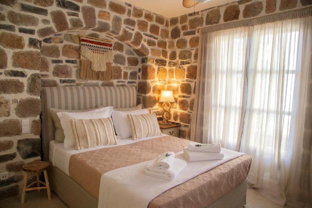 1 dormitorio con 1 cama grande y pared de piedra en Lithos Residence Poros en Poros