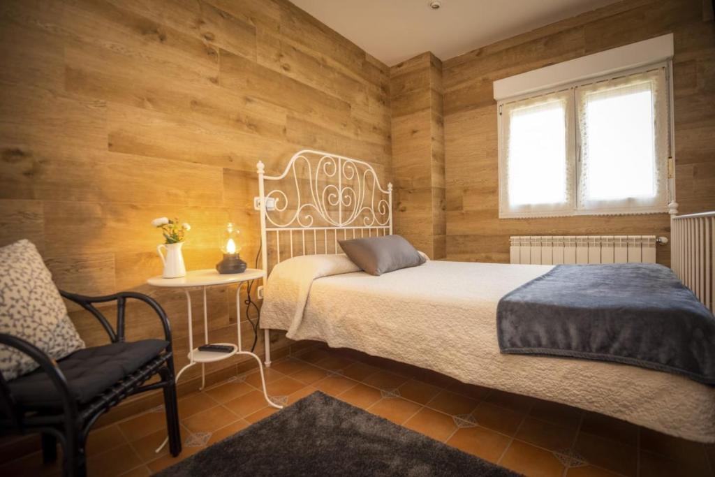 a bedroom with a bed and a chair and a window at Apartamentos Pumarin in Santa Marina