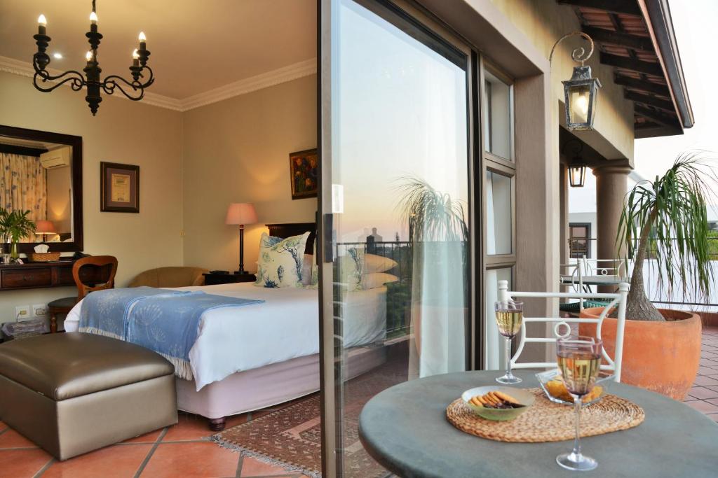 The Vineyard on Ballito في باليتو: غرفة نوم مع سرير وطاولة مع كؤوس للنبيذ
