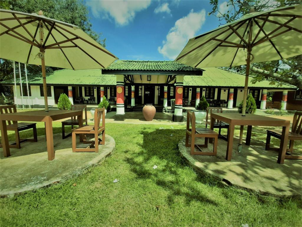 Dambulla Heritage Rest House في دامبولا: مجموعة طاولات ومظلات امام المبنى